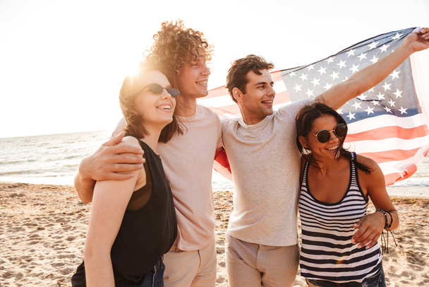 Image d'un heureux groupe d'amis à l'extérieur sur la plage tenant drapeau des États-Unis s'amusant
. - Photo, image