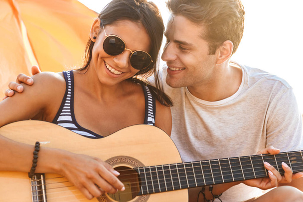 かわいいお友達と愛するカップル屋外でギターをプレイしながら座っているビーチの画像. - 写真・画像