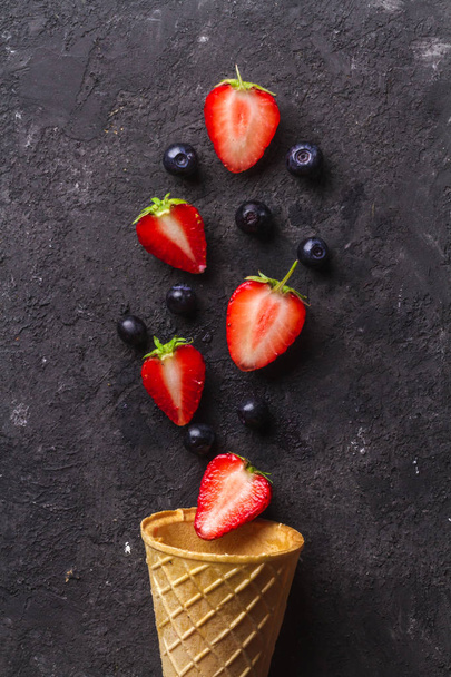 Crispy waffle cone with blueberries and strawberries on black background. Copy space. - Фото, изображение