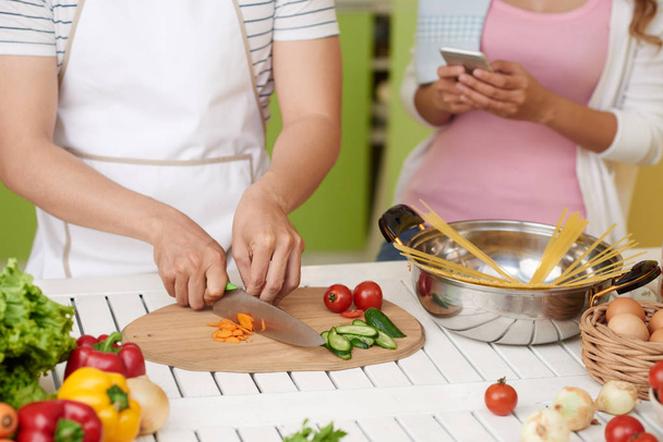 Cropped image of young man making salad when his is girlfriend using mobile app - Foto, Imagen