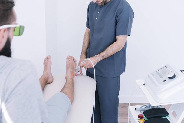The physiotherapist treating a man using equipment for Lightning Laser - Photo, Image