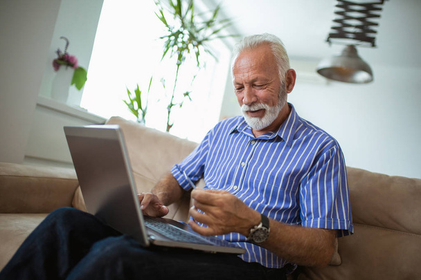 Старший чоловік робить онлайн покупки, сидячи вдома
 - Фото, зображення