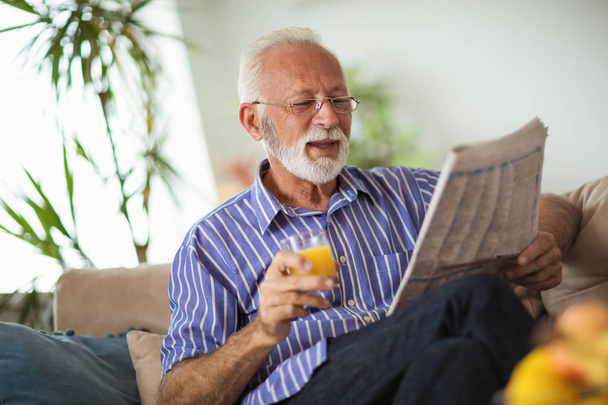 Senior férfi otthon olvasó újság és a gazdaság a friss gyümölcslé - Fotó, kép