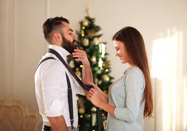 Woman clothe her boyfriend tie on the background Christmas tree at home - 写真・画像