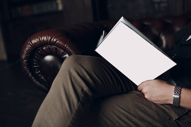 Мужчина читает книгу с белым чехлом на кожаном коричневом стуле
 - Фото, изображение