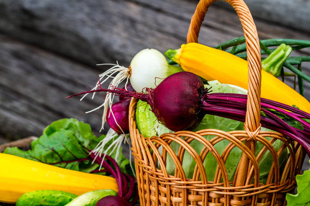 Freshly harvested vegetables in rustic wicker basket on wooden background - Foto, Imagen