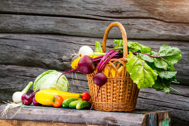 Fresh zucchini, cucumbers, onions, beets, tomatoes, cabbage in wicker basket on wooden background. Harvesting vegetables - Photo, Image