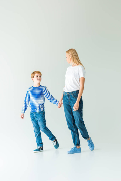 mother and son in casual clothes holding hands and looking at each other on white - 写真・画像