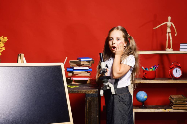 Girl holds microscope and stands by blackboard, copy space - 写真・画像