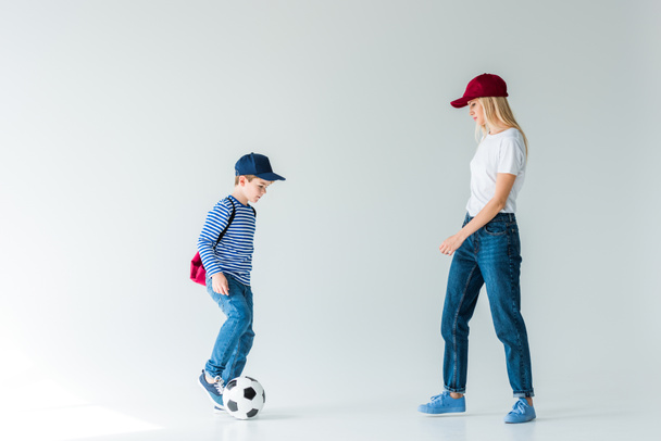 vista laterale di madre e figlio con zaino che giocano con pallone da calcio su bianco
 - Foto, immagini