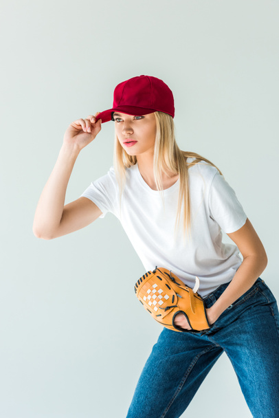 привабливий бейсболіст торкається червоної шапки і тримає бейсбольну рукавичку ізольовано на білому
 - Фото, зображення