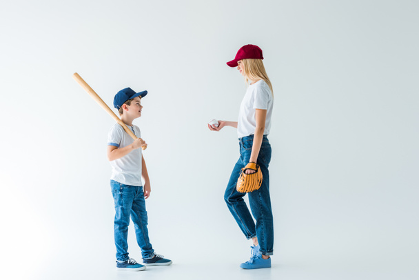 matka a syn stál s baseballovou pálkou, rukavice, míče a díval se na sebe na bílém - Fotografie, Obrázek