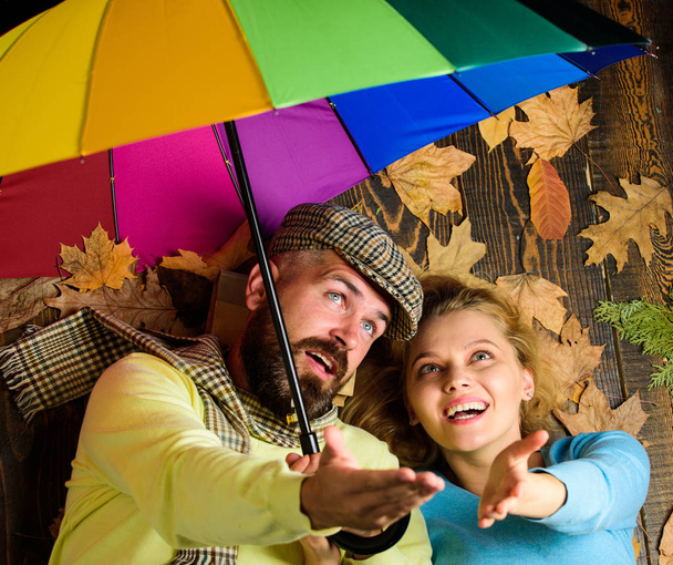 Rainy weather not obstacle for them. Couple dating. Hipster with beard and cheerful girl expect rainy weather hold colorful umbrella. Man bearded and blonde woman lay on wooden background top view - Foto, Bild