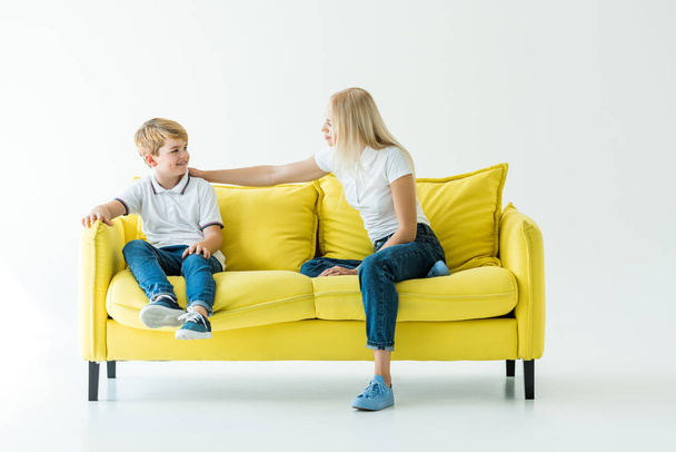 mother and son sitting on yellow sofa and looking at each other on white - Foto, Bild