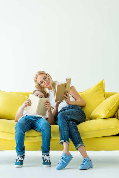 mother and son reading books together on yellow sofa - Foto, imagen