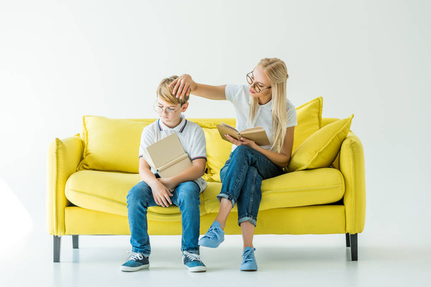 mother touching son hair while he reading book on yellow sofa - 写真・画像
