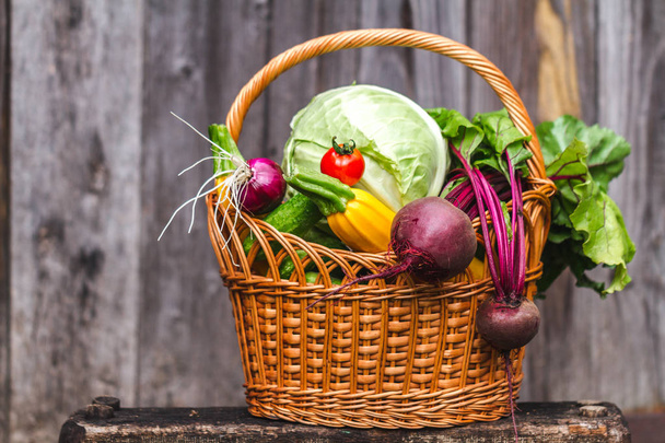 Fresh vegetables in basket on small chair on wooden background. - Foto, afbeelding