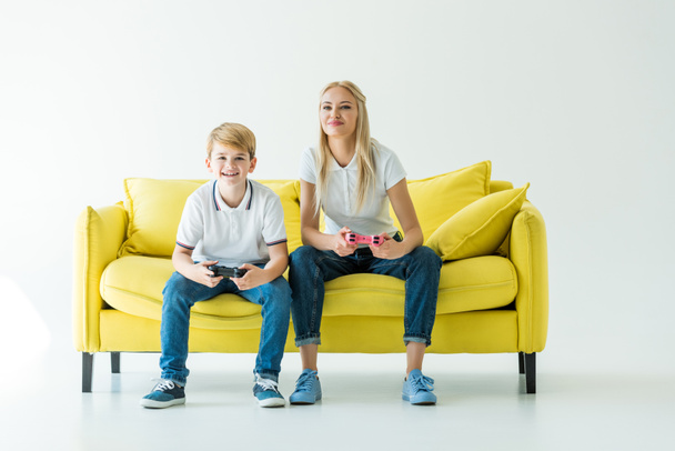cheerful mother and son playing video game on yellow sofa on white - Photo, Image