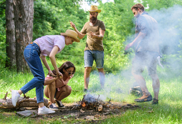 Company friends or family making bonfire in forest nature background. Friends working as team to keep bonfire. Add some wood to fire. Company camping forest prepare bonfire for picnic - Zdjęcie, obraz