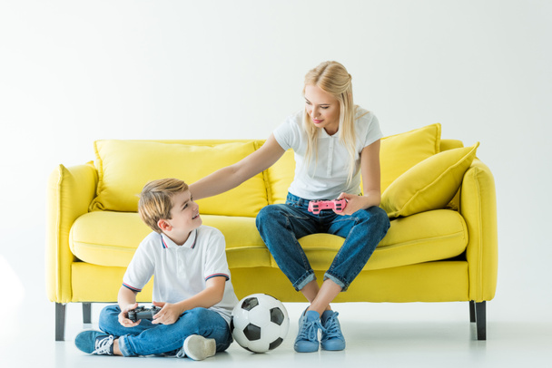 mère palming fils tout en jouant jeu vidéo sur canapé jaune sur blanc, ballon de football sur le sol
 - Photo, image
