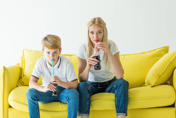 mãe e filho bebendo refrigerante saboroso com palhas no sofá amarelo isolado no branco
 - Foto, Imagem