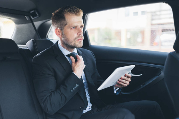 Executive businessman sitting at the back of car using a digital tablet - Foto, immagini