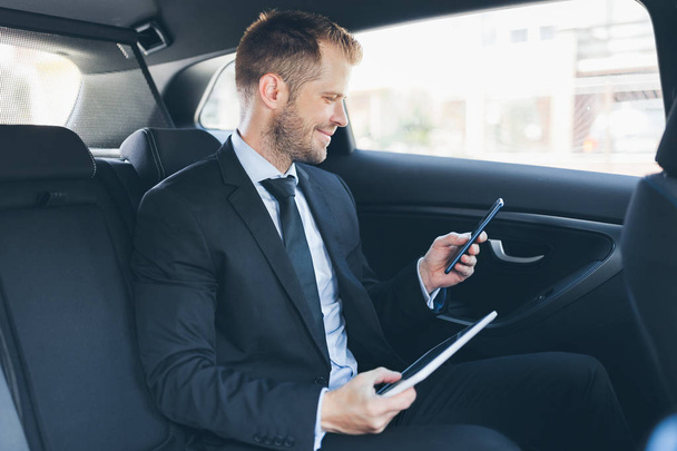 Executive üzletember ül a hátsó autó a mobiltelefon használata - Fotó, kép