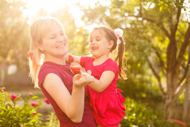 Gelukkig moeder en haar dochter hebben leuk eten aardbeien in zonnige boomgaard tuin  - Foto, afbeelding
