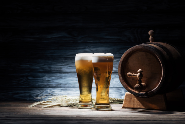 two glasses of beer, wheat spikelets and beer barrel on wooden table, oktoberfest concept - Foto, imagen