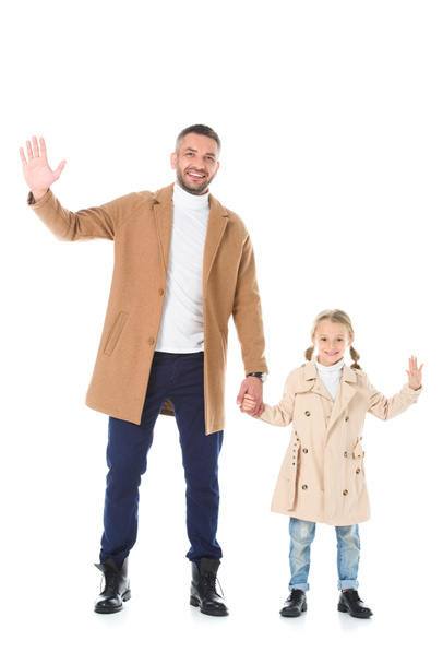 κομψό πατέρας και κόρη σε μπεζ παλτό, κρατώντας τα χέρια και κουνώντας απομονωθεί σε λευκό - Φωτογραφία, εικόνα
