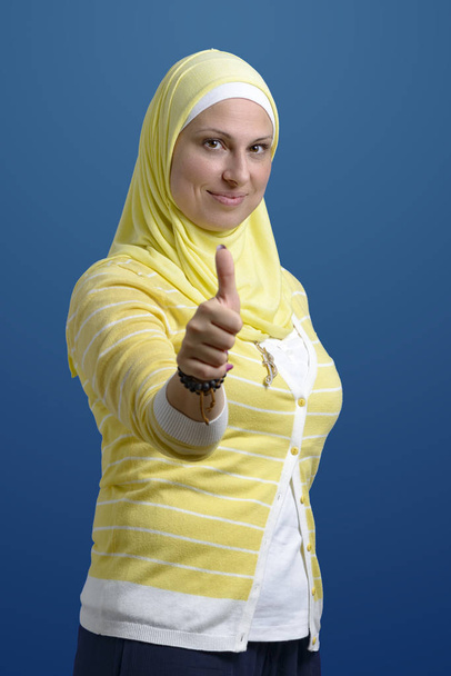 Polegares para cima bela mulher muçulmana sobre fundo azul
 - Foto, Imagem
