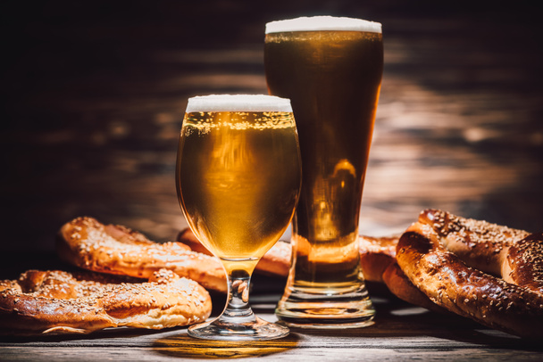 twee glazen van bier en smakelijke pretzels op houten tafel, oktoberfest concept - Foto, afbeelding