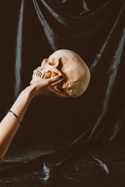 cropped view of woman holding halloween skull on black cloth - Фото, изображение