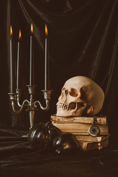 halloween skull on ancient books with black pumpkin, apple and candles on black cloth - Fotó, kép