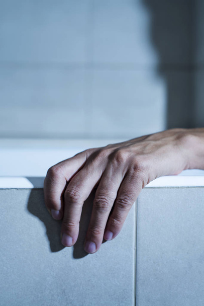 closeup of the hand of a young caucasian man on the side of a bathtub, in a mysterious atmosphere, with a dramatic effect - Photo, Image