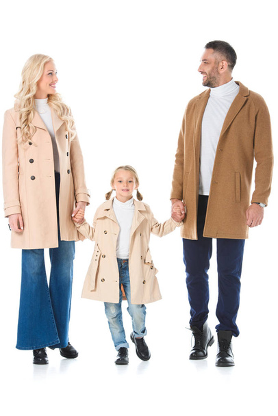 beautiful parents holding hands with daughter and posing in beige autumn coats, isolated on white - Foto, Imagem
