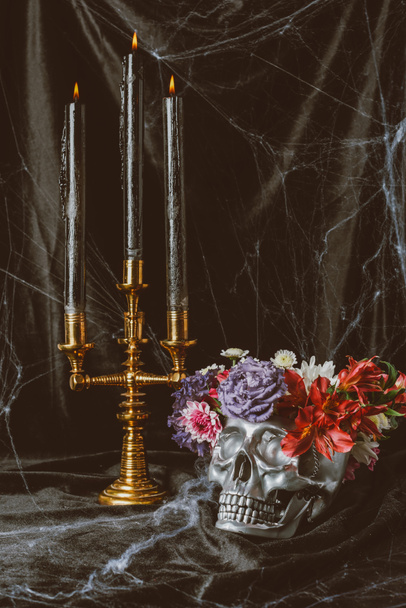 silver skull with flowers and candelabrum with candles on black cloth with spider web for halloween - Foto, imagen