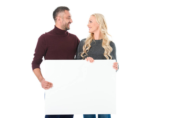 couple in autumn outfit holding empty placard and looking at each other, isolated on white - Foto, afbeelding
