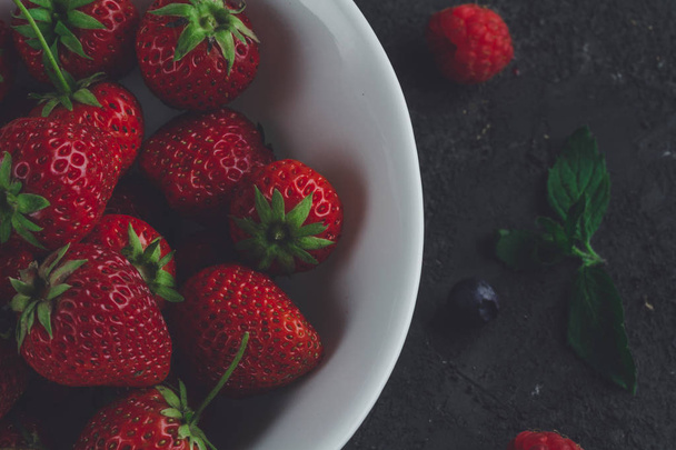 Fresh strawberries in white bowl on dark background - Fotoğraf, Görsel