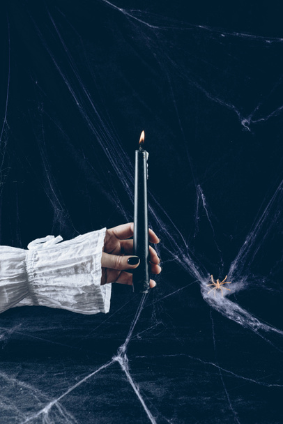 cropped view of scary woman holding black candle in darkness with spider web - Fotó, kép