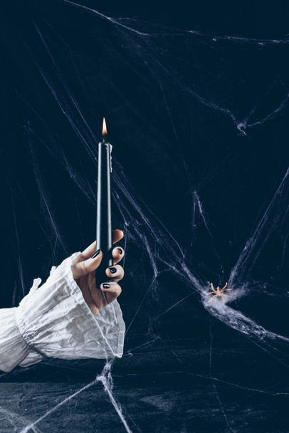 partial view of creepy woman holding black candle in darkness with spider web - Foto, Imagen