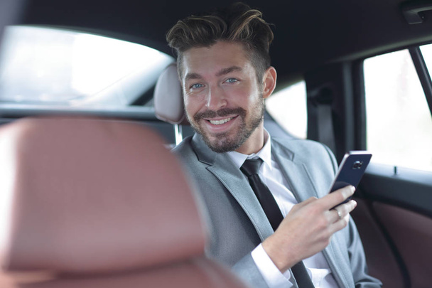 Unsmiling businessman sitting in the back seat in his car - Фото, изображение