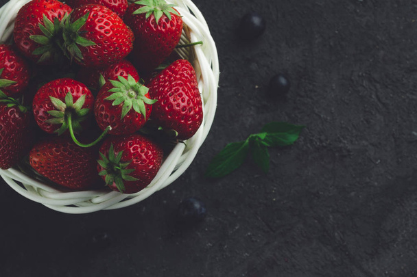 Fresh strawberries and blueberries in white basket on black background. Vitamins. Sweet berries. - Foto, afbeelding