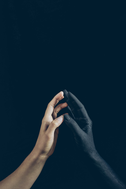 cropped view of woman touching with black demon hand isolated on black - Foto, Imagen