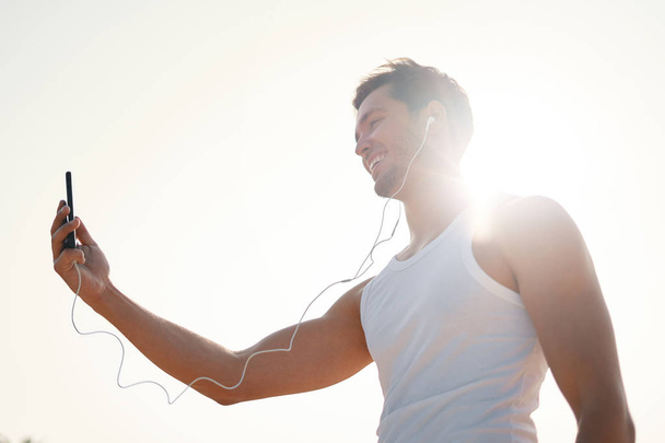 Handsome, happy, smiling young man having an online video chat using smartphone while walking, jogging outdoors on a sunny, beautiful day. Making selfie. Side view. White background. - Foto, imagen