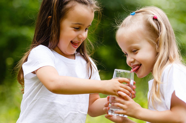 Dos niñas bebiendo un vaso de agua en el parque verde. Concepto de pureza, producto ecológico y biológico, amor por la naturaleza
 - Foto, Imagen