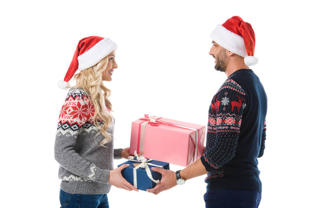 couple in christmas sweaters and santa hats gifting presents, isolated on white - Foto, afbeelding