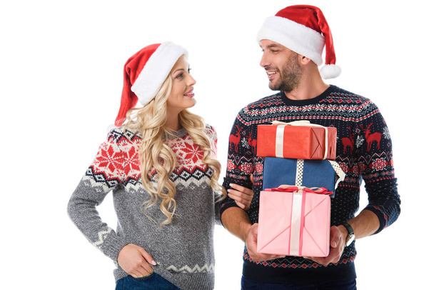happy couple in christmas sweaters and santa hats holding presents, isolated on white - Fotografie, Obrázek