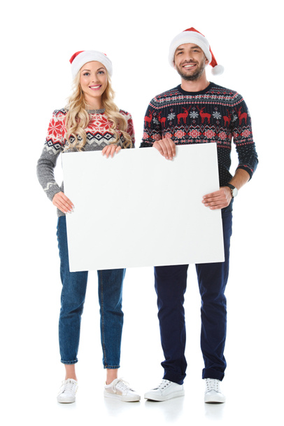 クリスマス セーターとサンタ帽子白で隔離、空白のカードを持っている幸せなカップル - 写真・画像