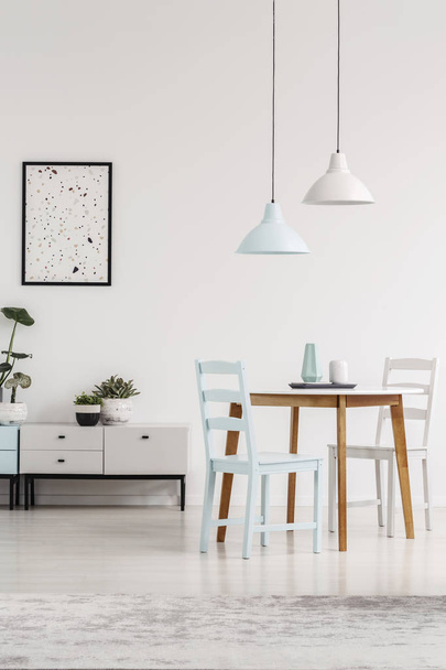 Lamps above table and chairs in pastel dining room interior with poster above cupboard. Real photo - Fotó, kép